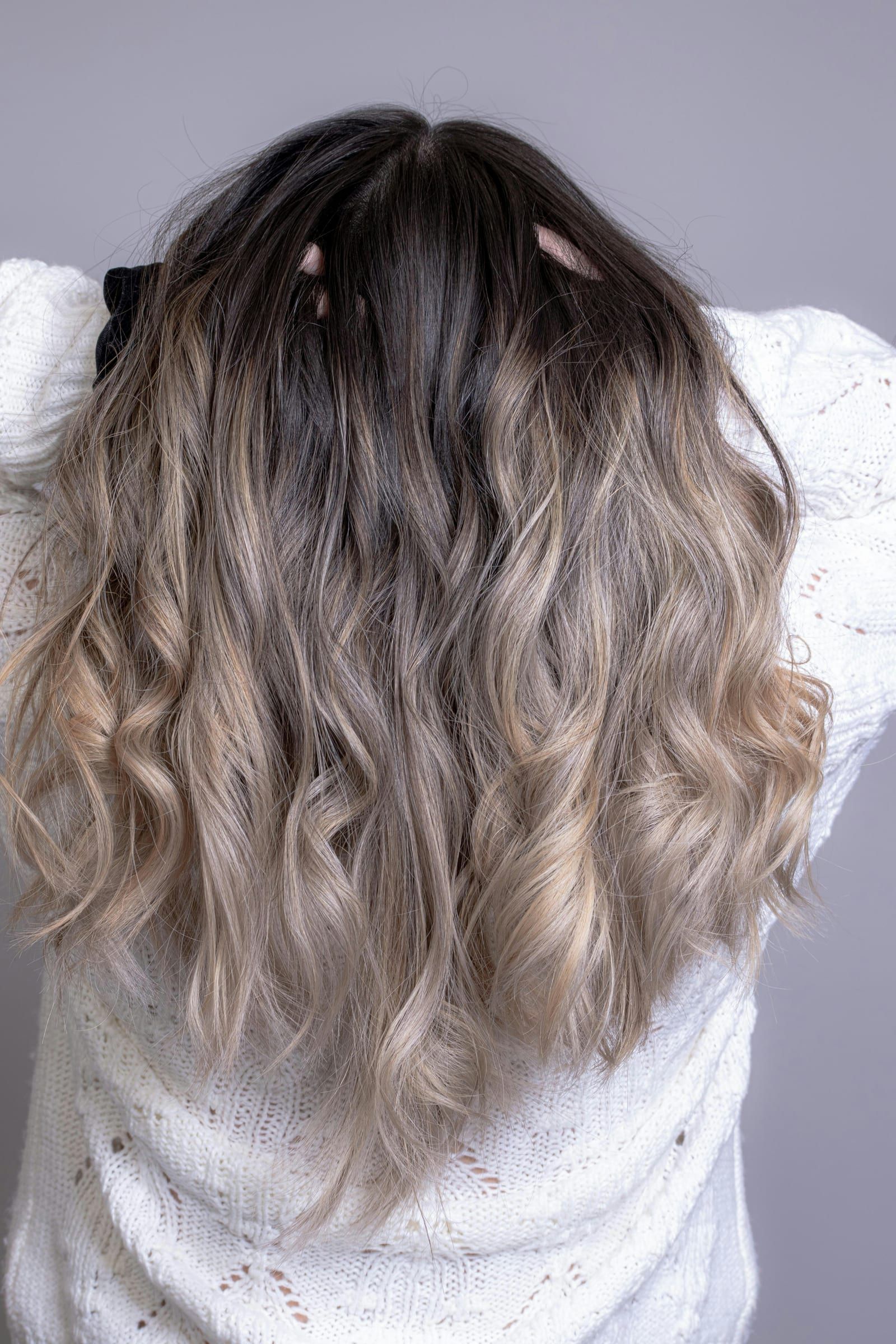 Long waved hair melting from a dark root into soft ash blonde ends