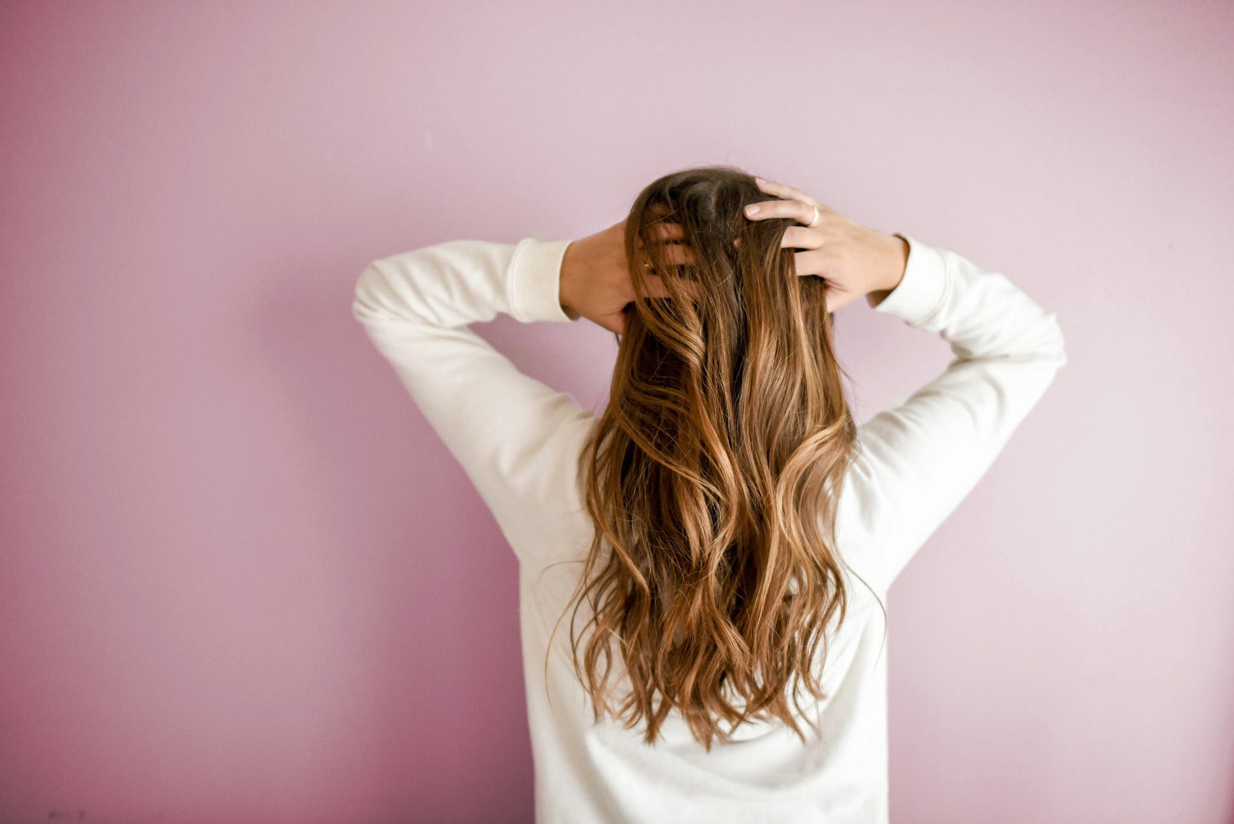 Long brunette hair with warm caramel balayage, falling in loose waves against a pink wall