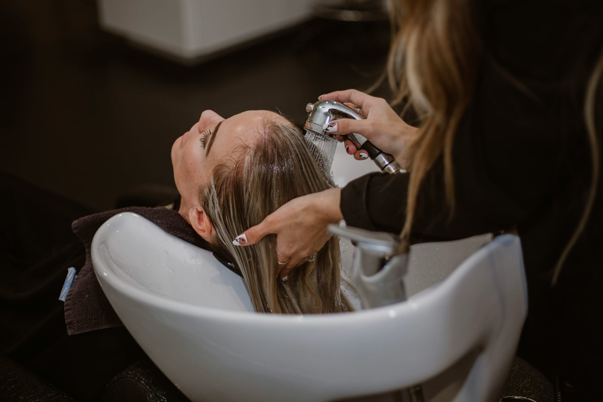 A client relaxing at the basin with her eyes closed while her blonde hair is rinsed