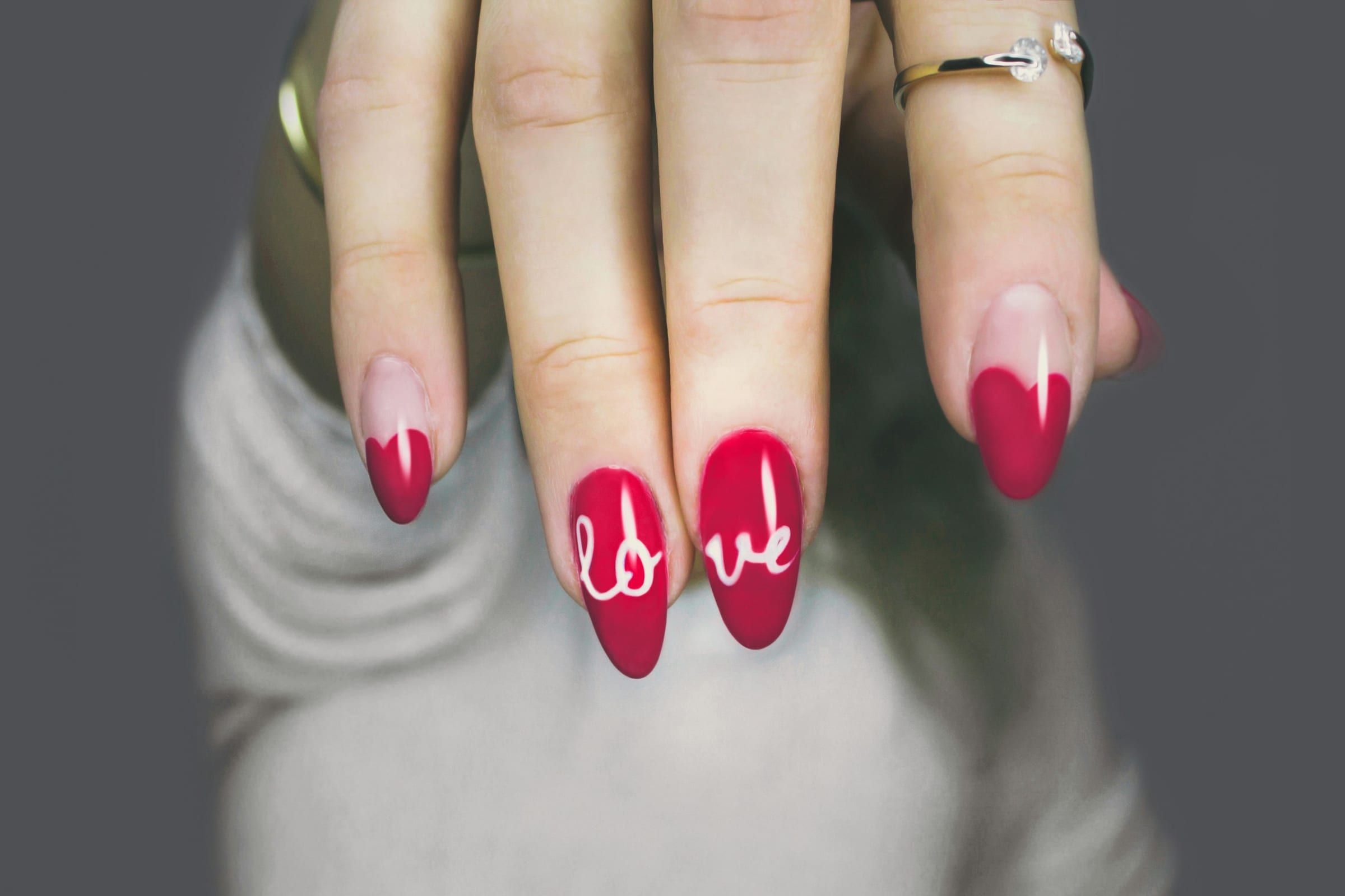 Almond-shaped red gel nails with heart tips and the word love painted in white